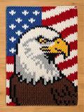 A chunky knit blanket featuring a bold American flag design with a detailed bald eagle head in the center, showcased flat on a light wooden background.