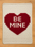 Chunky knit cream blanket featuring a large red heart in the center with the text "BE MINE" knitted inside