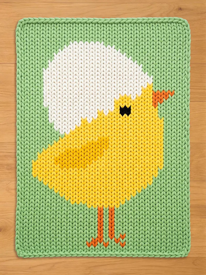 Flat lay of a chunky knit baby blanket featuring a cute yellow chick with a white eggshell on its head, knitted into a mint green background