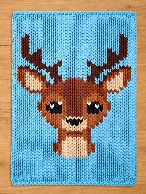 A knitted blanket featuring a pixelated deer design. The deer has brown antlers, a brown body, and a beige face. The background is a solid light blue color. The blanket is made of a soft, chunky knit material.