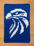 A knitted blue and white decorative square with a stylized design. The design features a white abstract eagle shape against a solid blue background. The item is made of a thick, textured yarn.
