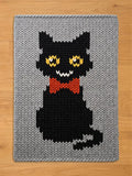 Chunky knit blanket in light gray featuring a knitted black cat pattern with a red bow tie and yellow eyes.