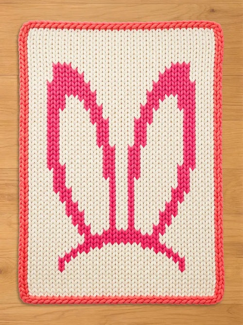 Chunky knit blanket featuring a pink bunny ears pattern on a cream white background with a pink braided border.