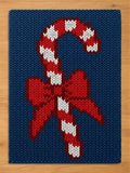 A chunky knit blanket featuring a large red and white striped candy cane with a red bow, knitted into a deep blue background.