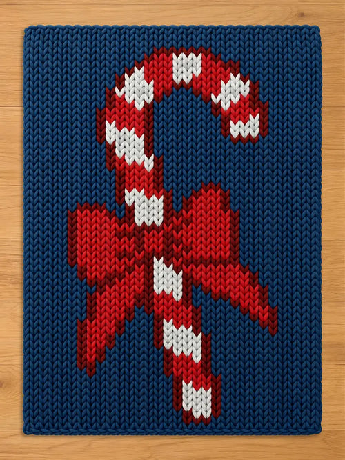 A chunky knit blanket featuring a large red and white striped candy cane with a red bow, knitted into a deep blue background.