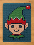 Chunky knit Christmas elf blanket featuring a woven pattern of a smiling elf face with a green pointed hat on a dark blue background