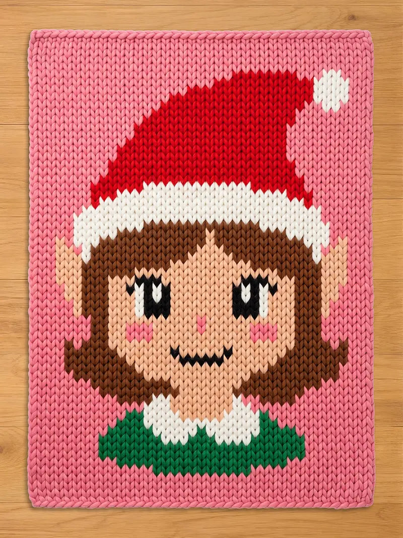 A rectangular knit blanket featuring a pink background and a central graphic of an elf face. The elf wears a red and white Santa hat with a white pom-pom, has brown hair, pointed ears, rosy cheeks, and a green collar with white trim.