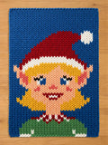 A chunky knit blanket featuring a woven Christmas elf girl design with blonde hair, a red Santa hat, and a green shirt against a solid blue background.
