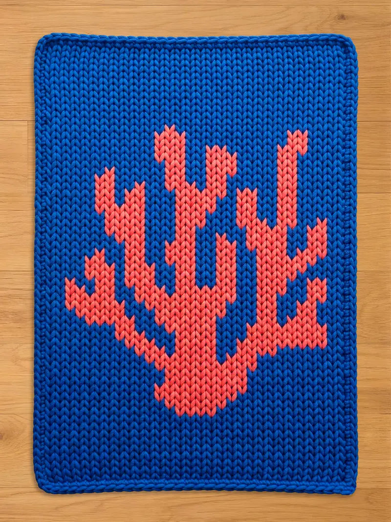 A knitted chunky blanket in a vibrant blue color. The design features a coral-like pattern in a contrasting coral-red hue. The edges are neatly finished, creating a clean, modern look.