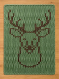 A rectangular knit blanket featuring a large, centered deer head graphic. The design is created with dark brown yarn stitches against a solid sage green background, showcasing a clear, geometric outline of antlers and a snout.
