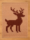 Chunky knit blanket in beige featuring a large brown stag deer silhouette pattern, displayed flat on a wooden surface.