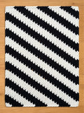 A black and white knitted chunky blanket with a bold diagonal stripe pattern. The blanket is rectangular and features thick, textured stripes. The contrasting colors create a striking visual effect, suitable for home decor.