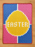 Chunky knit blanket featuring a yellow Easter egg design with the word "EASTER" in white, set against a pink and blue color-blocked background.