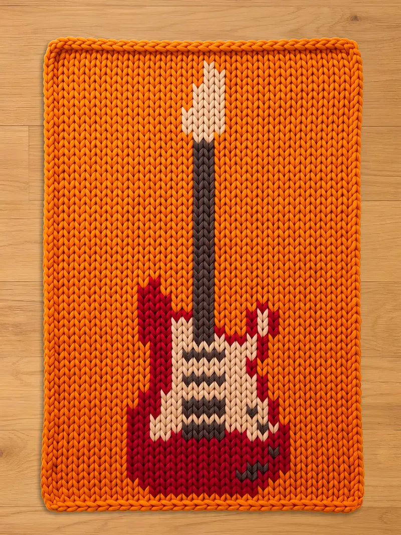An orange knitted rectangular chunky blanket featuring a red, white, black, and gray electric guitar design. The guitar has a black neck and a white headstock. The blanket  is made of thick yarn.