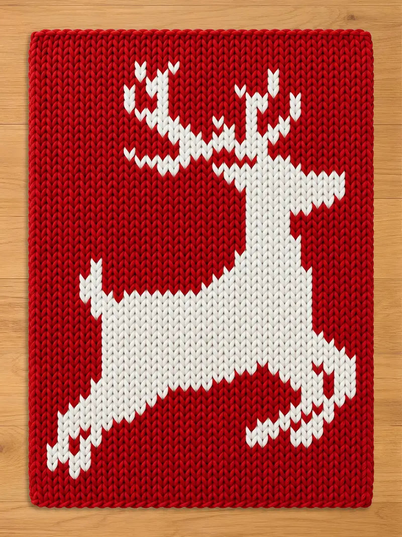 Cozy red chunky knit Christmas blanket with a woven white flying reindeer design in the center, displayed flat on a wooden background.