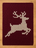 Maroon and cream chunky knit reindeer blanket with a holiday silhouette pattern, styled flat on a wooden background for a cozy winter aesthetic.