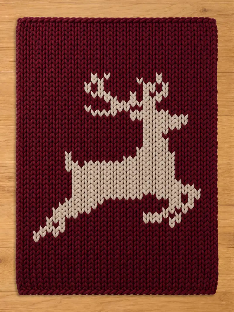 Maroon and cream chunky knit reindeer blanket with a holiday silhouette pattern, styled flat on a wooden background for a cozy winter aesthetic.