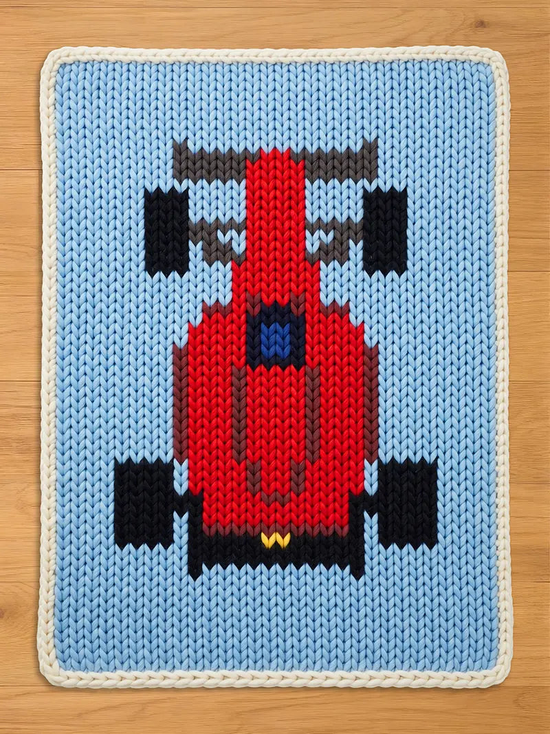 Chunky knit blanket featuring a red Formula 1 race car design on a light blue background with a white braided border.