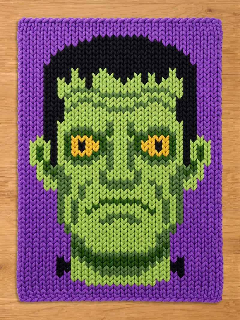 A chunky knit blanket featuring a green Frankenstein monster face with yellow eyes, black hair, and a purple background.