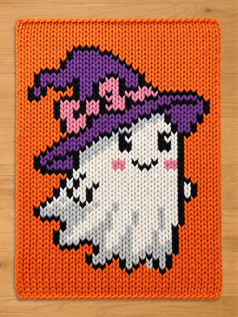 A rectangular knit blanket featuring a vibrant orange background with a central graphic of a white ghost wearing a purple witch hat with pink accents. The ghost has black eyes, a black mouth, and pink cheeks, all rendered in knit.