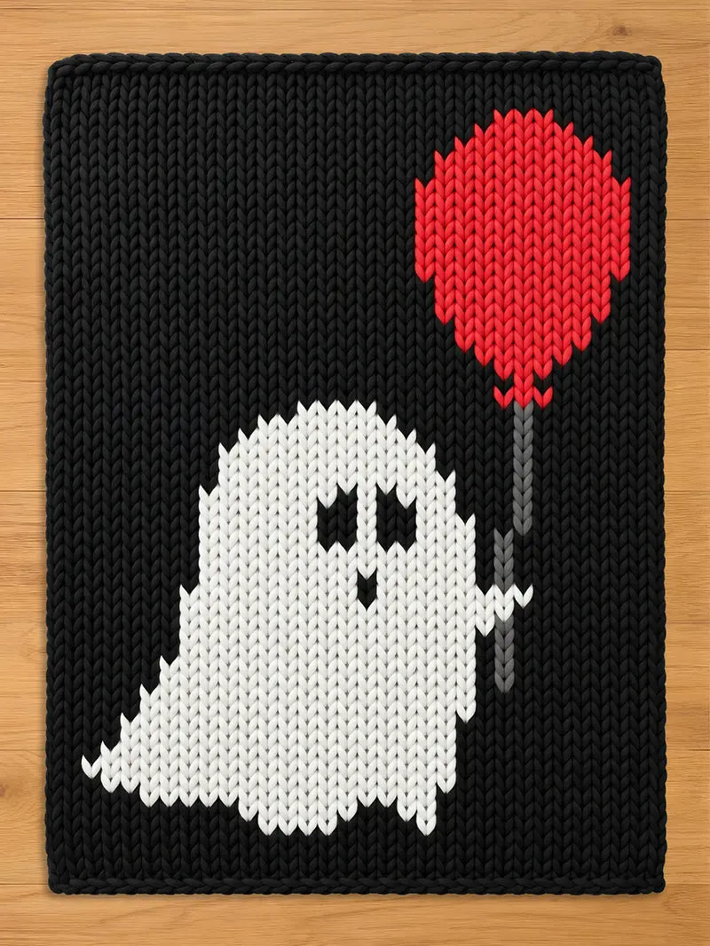 A rectangular knit blanket featuring a black background with a white ghost character in the center. The ghost has two black eyes and a small black mouth, and it is holding a red balloon attached to a grey string.