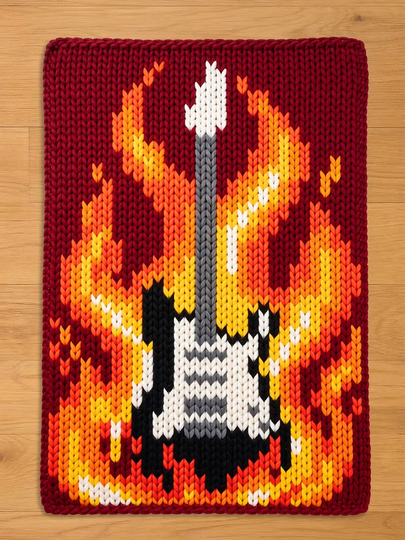 A knitted guitar design with flames in shades of yellow, orange, and red. The guitar is black, white, and gray, set against a burgundy background. The image is a close-up of a knitted item.