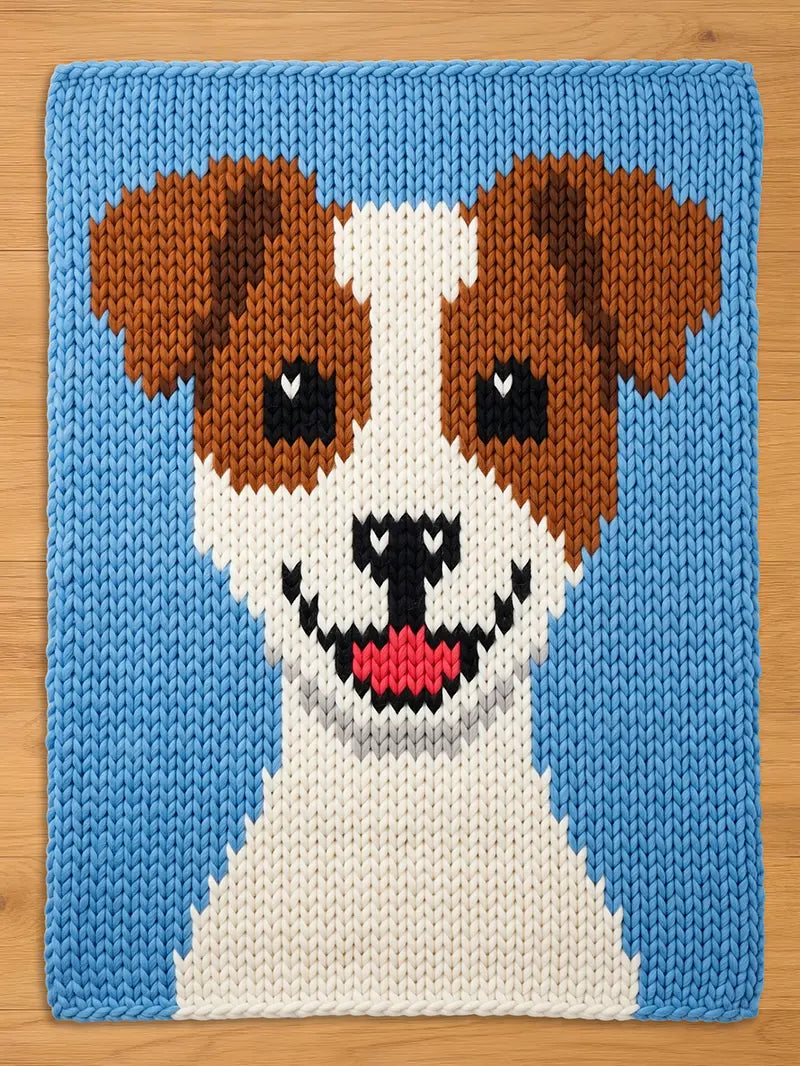 A knitted chunky blanket featuring a smiling dog face. The dog has brown ears, black eyes, and a white and brown face. The background is light blue, and the dog's mouth is pink. The square is made of yarn.