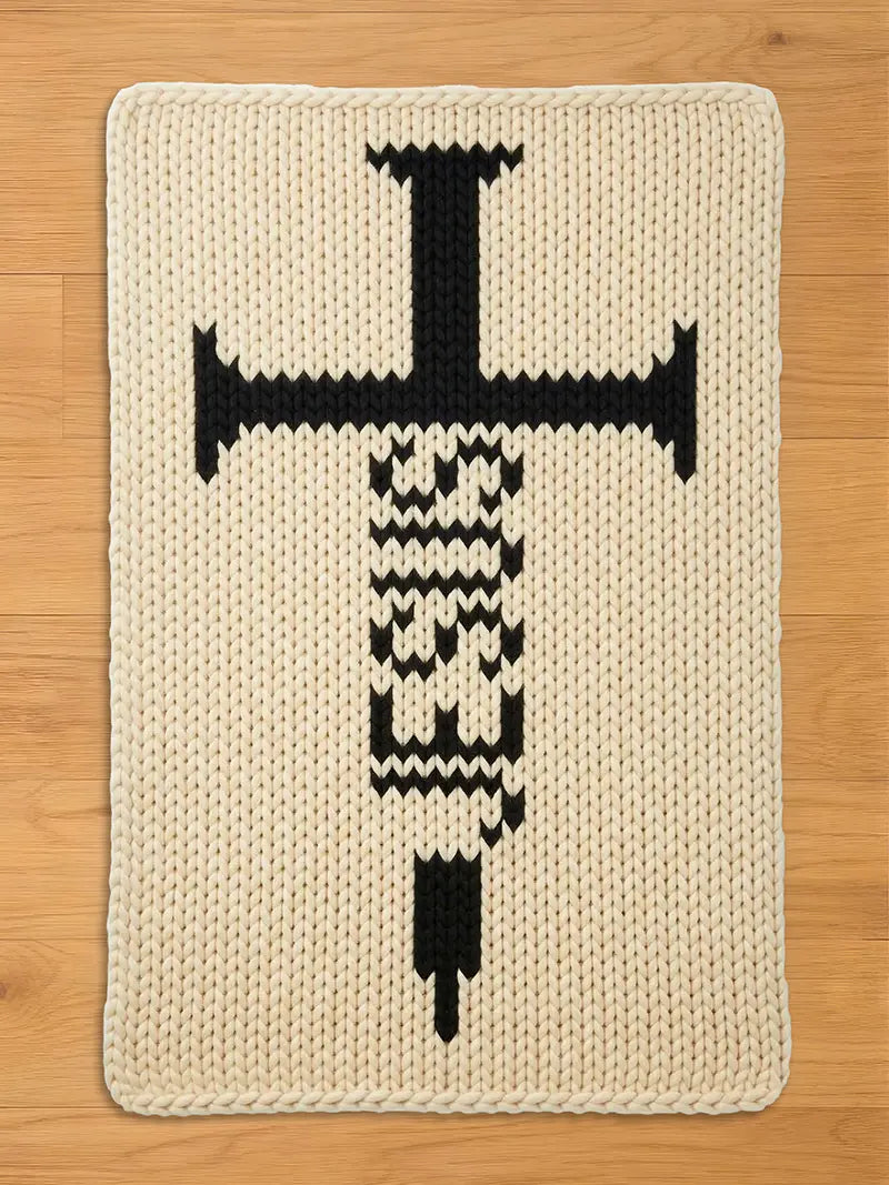 Cream-colored, knitted rectangular chunky blanket with a large black syringe design. The syringe features a cross-shaped top and a detailed body, creating a bold, graphic statement. The rug's texture is visible, adding depth to the design.