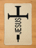 Cream-colored, knitted rectangular chunky blanket with a large black syringe design. The syringe features a cross-shaped top and a detailed body, creating a bold, graphic statement. The rug's texture is visible, adding depth to the design.