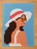  A rectangular knit blanket featuring a graphic design of a person in profile. The person has dark brown hair, wears a white sun hat with a coral band, and brown sunglasses. The background is light blue, and the person wears a white top.