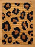 A rectangular knitted chunky blanket with a leopard print pattern. The blanket features a tan background with dark brown and light brown spots. The knitted texture is visible throughout the design.