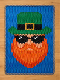 Chunky knit blanket featuring a leprechaun face with an orange beard, green top hat, and black sunglasses on a bright blue background