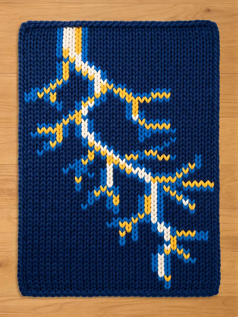 A navy blue knitted blanket with a lightning bolt design. The lightning bolt is white, yellow, and blue. The blanket is rectangular and appears to be made of thick yarn.