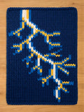 A navy blue knitted blanket with a lightning bolt design. The lightning bolt is white, yellow, and blue. The blanket is rectangular and appears to be made of thick yarn.
