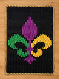 Chunky knit black blanket featuring a large Mardi Gras fleur-de-lis in green, purple, and yellow, finished with a gold braided border