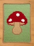 Chunky knit blanket featuring a large red mushroom with white spots on a light green background