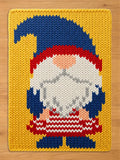 A rectangular knit blanket featuring a gnome graphic. The gnome has a large blue hat, a white beard, and a red and white striped shirt. The background of the blanket is yellow, and the gnome wears blue boots and blue mittens.