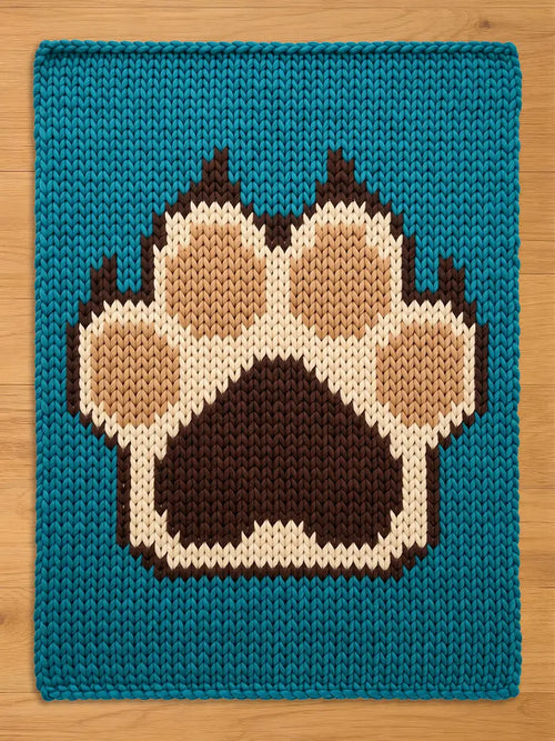 A knitted  chunky blanket with a teal background and a large paw print design. The paw print is made up of brown, tan, and cream-colored yarn, creating a textured and cozy appearance. The blanket is likely for a pet.