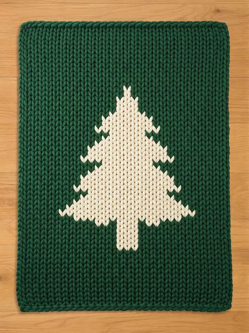 Dark green chunky knit blanket featuring a large, off-white pine tree silhouette pattern in the center, laid flat on a wooden surface
