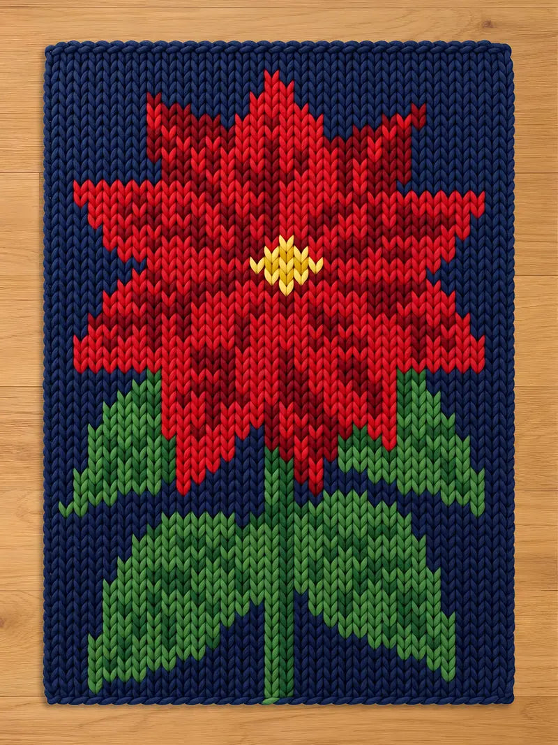 A rectangular chunky knit blanket featuring a dark navy blue background with a central poinsettia design. The flower has vibrant red petals with a small yellow center, and the stem and leaves are rendered in various shades of green.