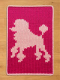 A chunky knit blanket in vibrant magenta pink featuring a light pink knitted poodle silhouette in the center, finished with a light pink border and displayed on a light wood floor.