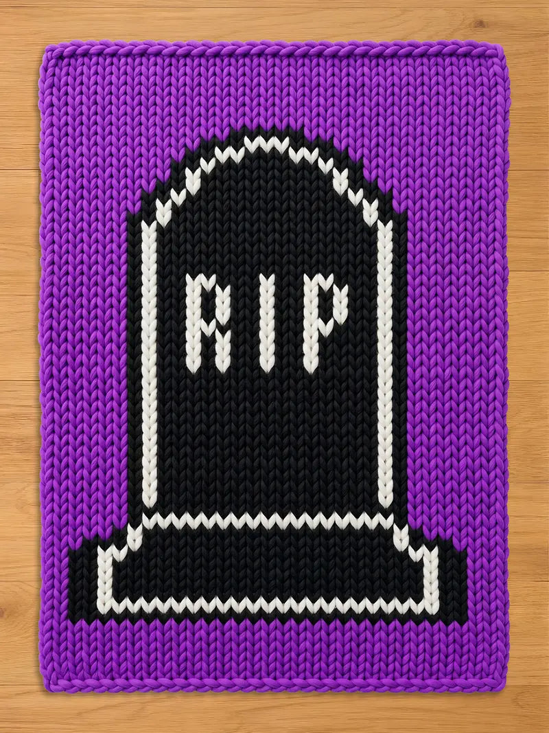 A rectangular knitted blanket featuring a purple border and a central black tombstone motif. The tombstone is outlined in white yarn and displays the white knitted text RIP in the center, with a white base detail at the bottom.
