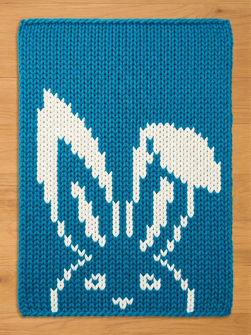 Chunky knit blue blanket featuring a white knitted rabbit pattern with long ears, laid flat on a light wood surface