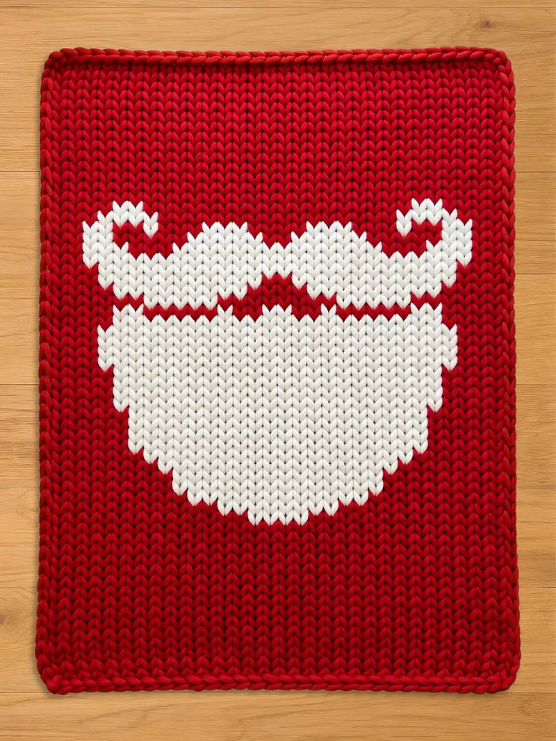 A red chunky knit blanket featuring a large, white knitted design of a Santa Claus beard and curled mustache in the center.