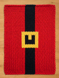 A knitted chunky blanket witth a black vertical stripe and a yellow square buckle. The design resembles Santa Claus's belt. The item is likely a decorative piece or a holiday-themed accessory.