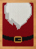 A chunky knit blanket designed to look like a Santa Claus suit, featuring a red background, a large white beard pattern at the top, and a black belt with a gold buckle near the bottom