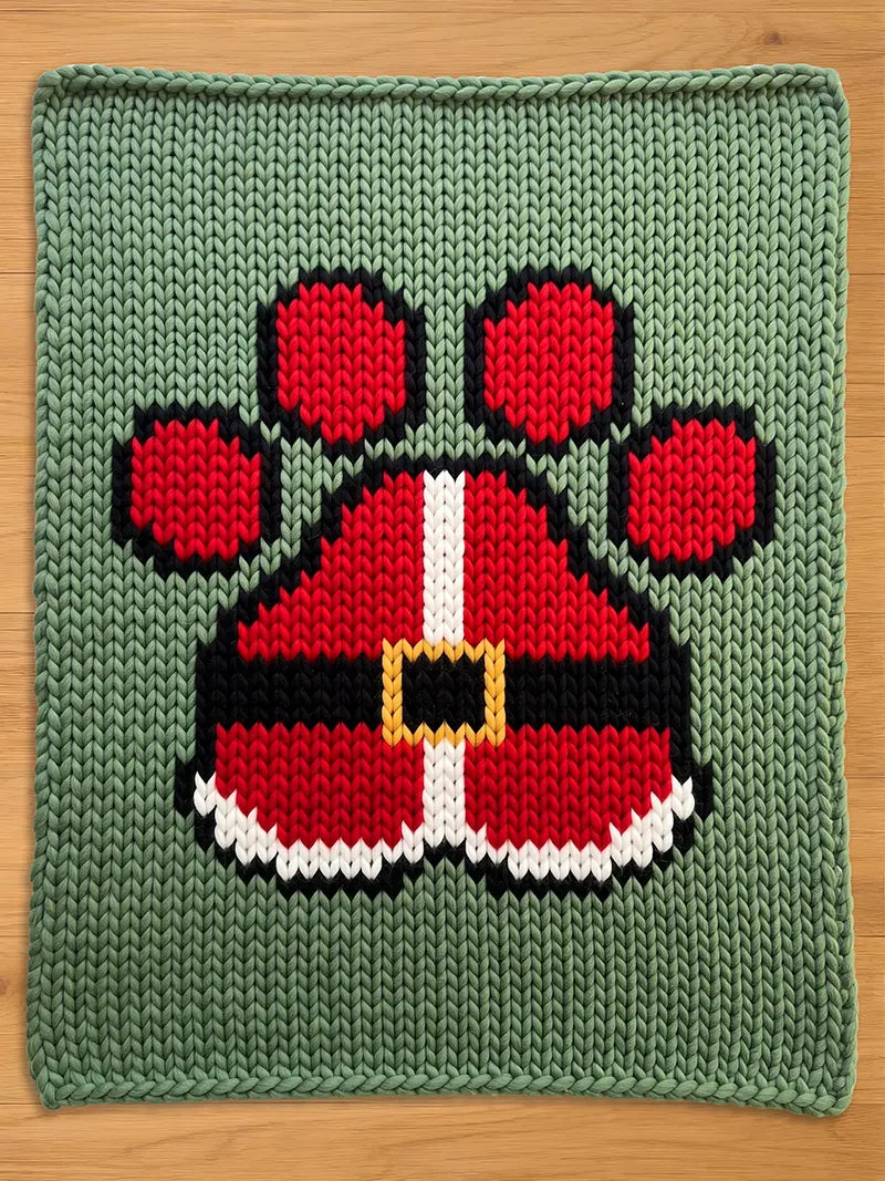 A knitted green chunky blanket with a Santa Claus paw print design. The paw print is red with black and white accents, and a gold buckle. The blanket is made of a soft, textured material.