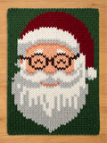 A chunky knit blanket featuring a large, colorful portrait of Santa Claus wearing glasses on a dark green background.