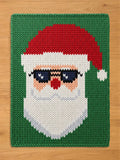 Chunky knit blanket featuring a pattern of Santa Claus wearing black sunglasses against a green background.