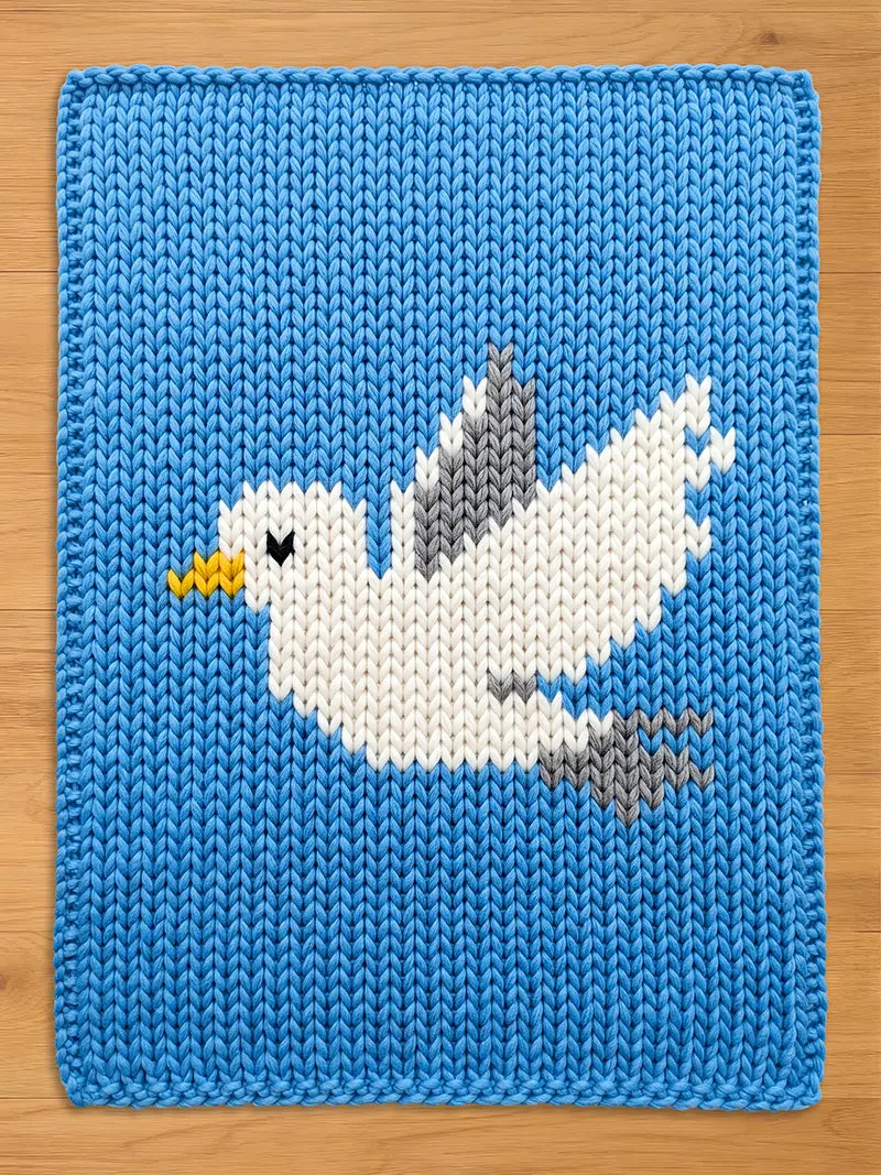 A knitted chunky blanket in a vibrant blue color, featuring a white seagull design with gray and yellow accents. The seagull is depicted in flight, adding a dynamic element to the textile art. The piece is likely a decorative item or a baby blanket.